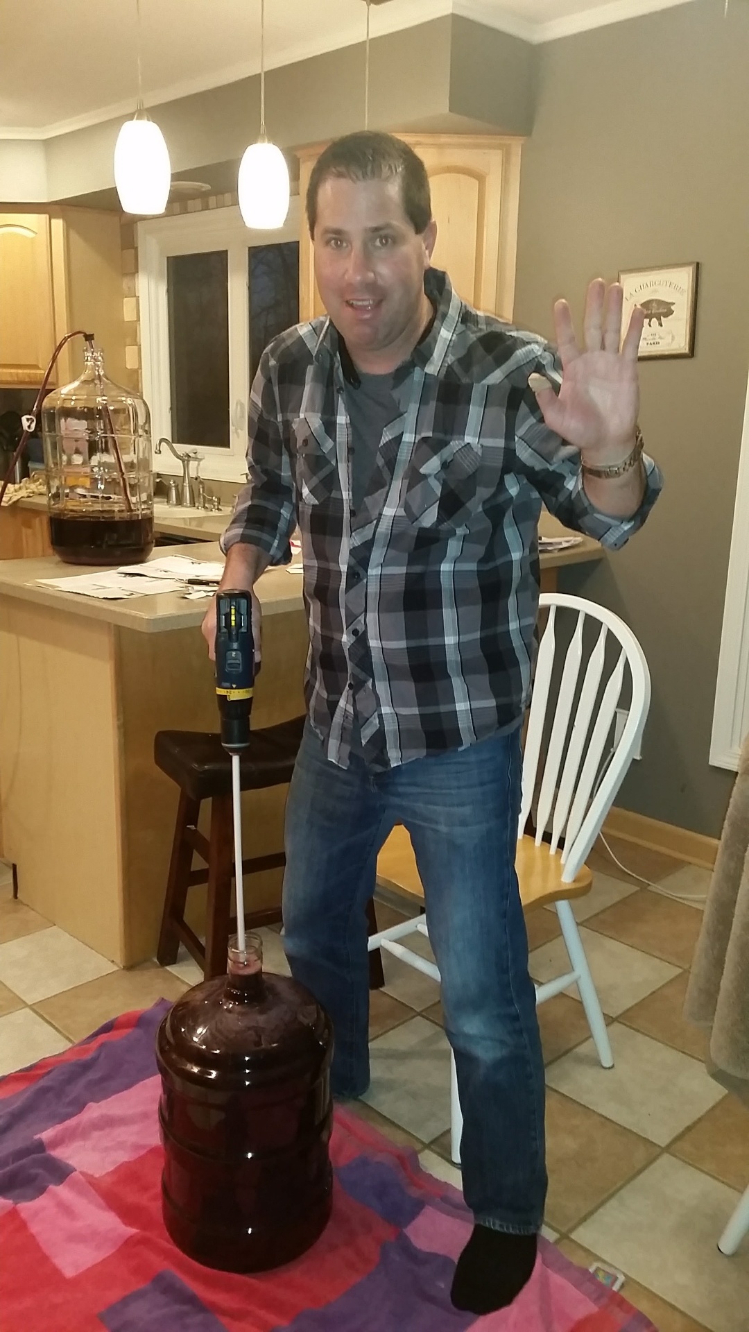 Russ in a plaid shirt grinning and waving while degassing a carboy of young Cabernet with a drill-mounted stirring rod