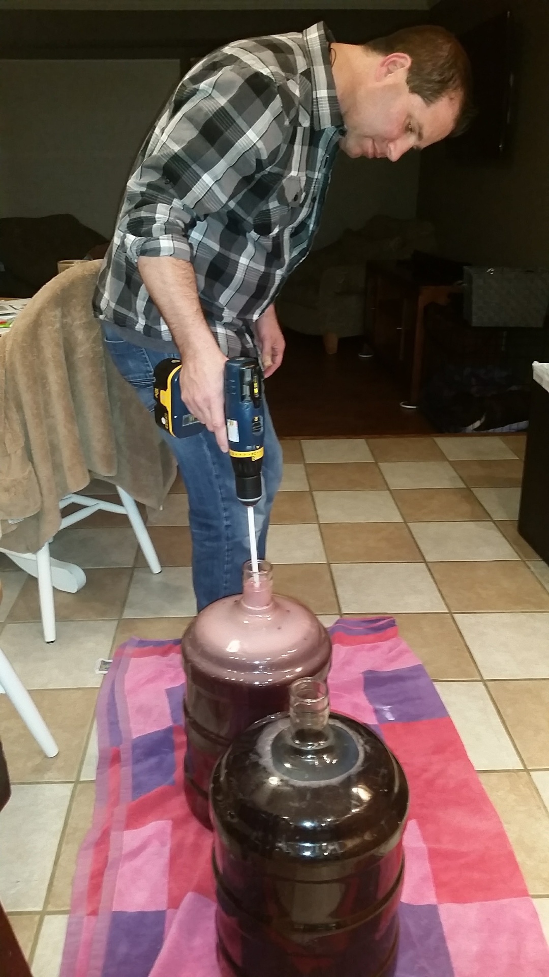 Close-up of Russ leaning over two carboys of pink and dark Cabernet, drill-stirring to degas