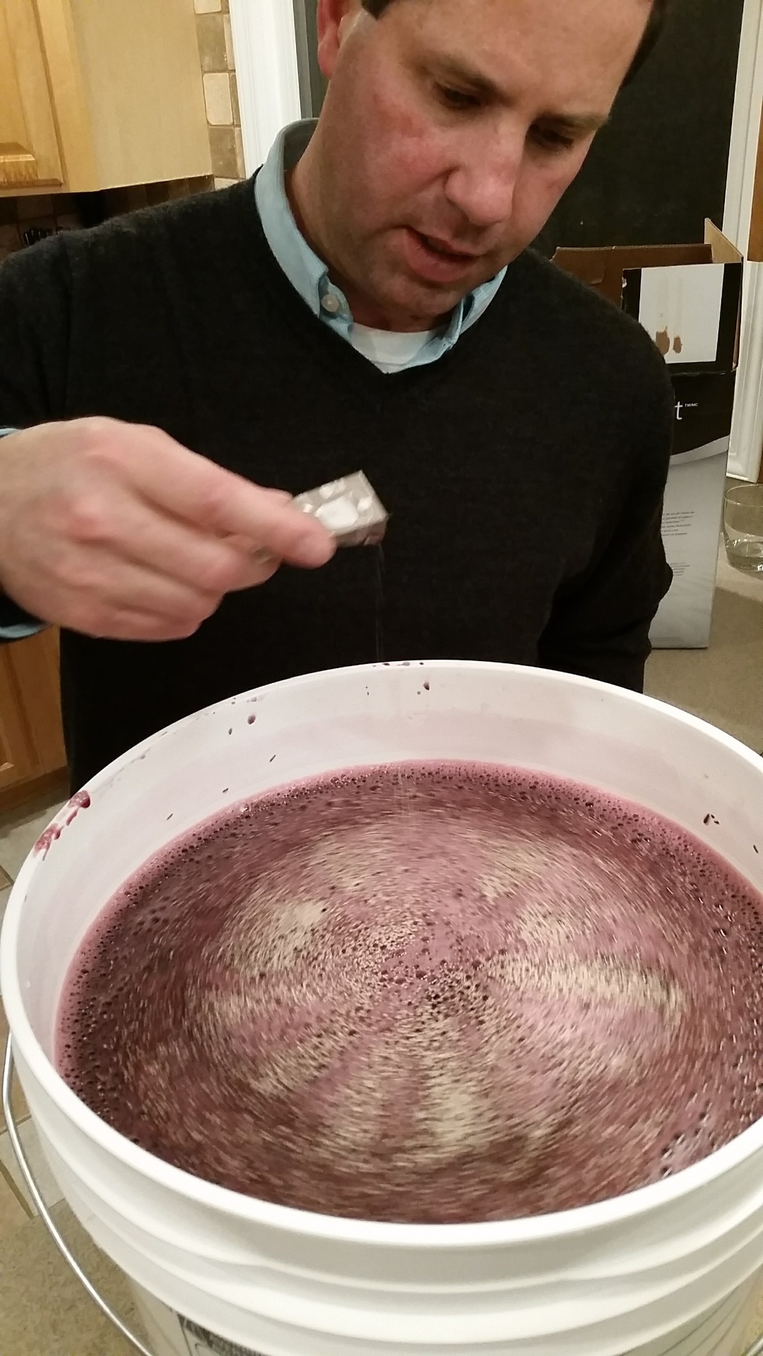 Russ sprinkling yeast onto the surface of a foamy purple Cabernet must in a primary fermenter