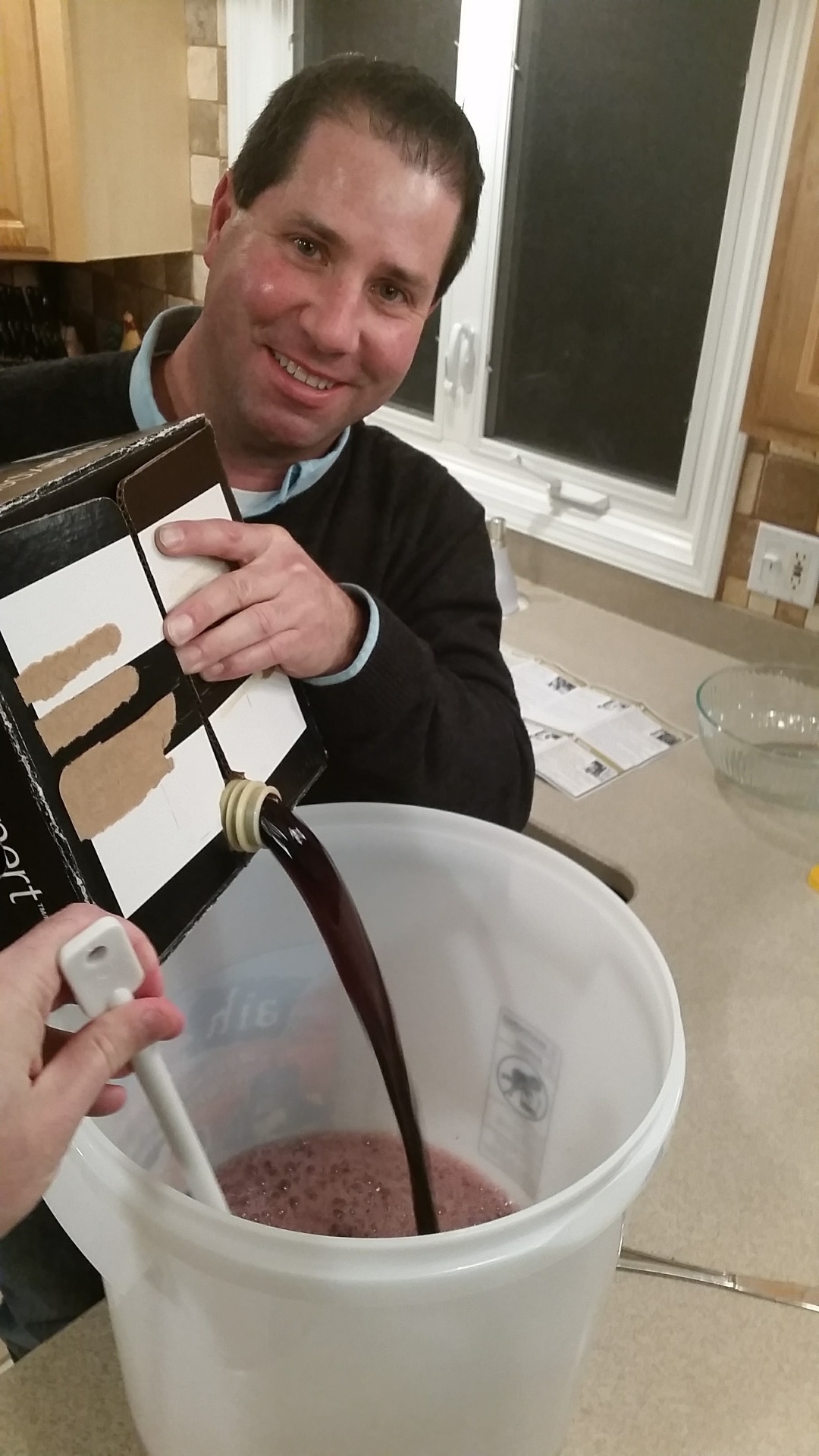 Russ smiling as he pours Cabernet kit juice from a bag-in-box into a primary fermenter — our very first Cabernet, 2016