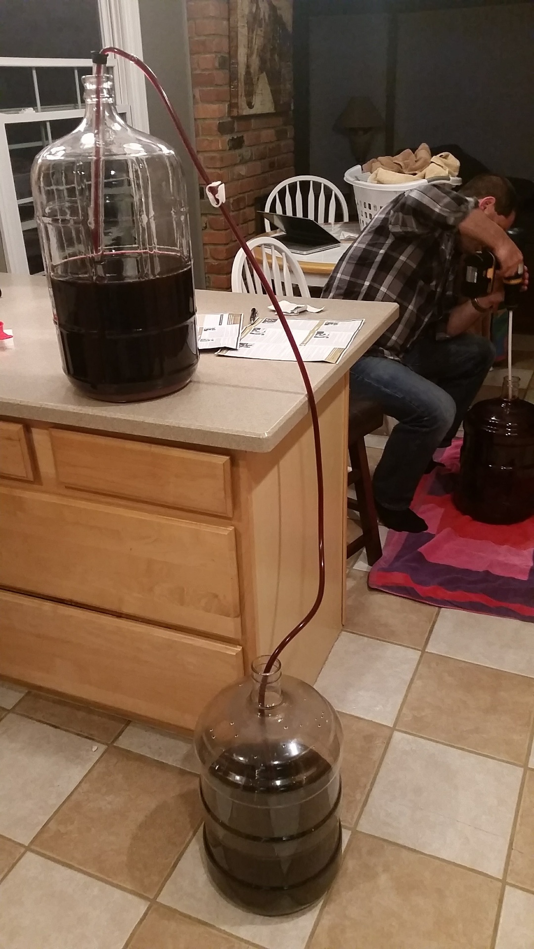 Cabernet being racked by siphon from a full glass carboy on the counter down to a smaller carboy on the floor, Russ working in the background