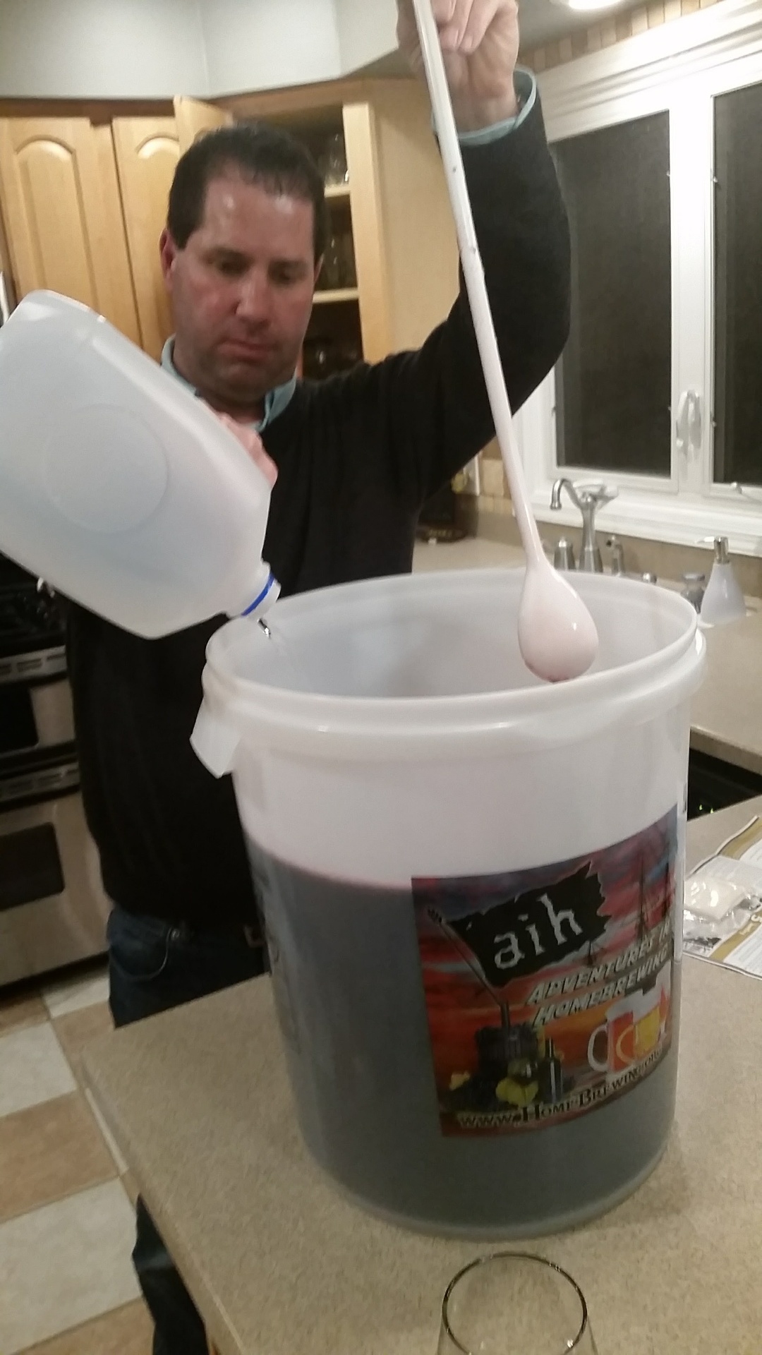 Russ stirring the primary fermenter with a long spoon while topping up water on our first Cabernet batch, 2016