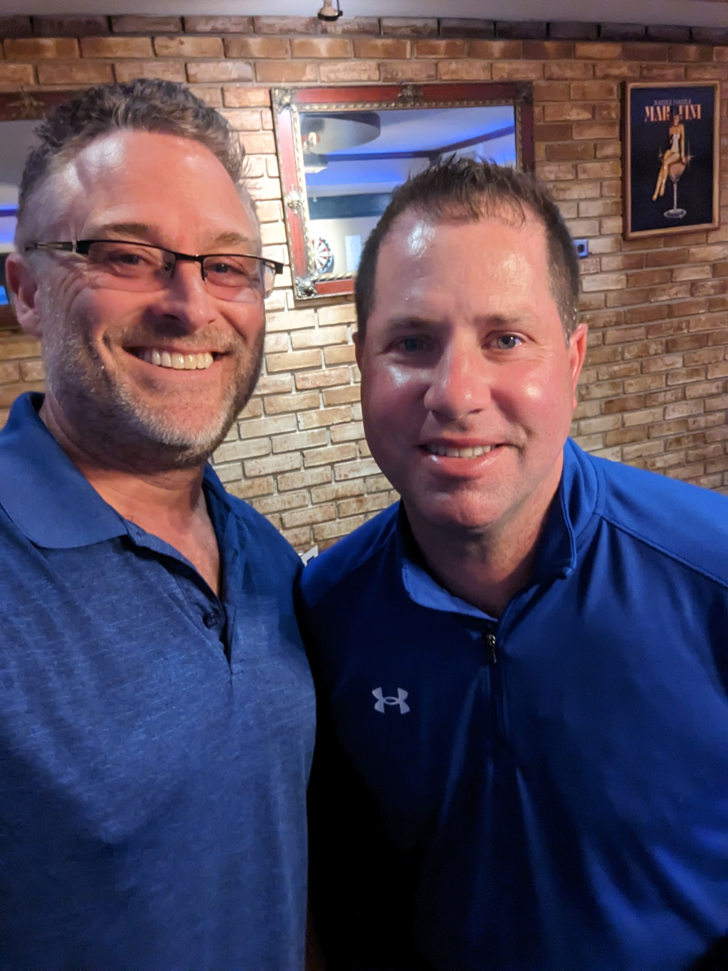 Todd (left, in glasses) and Russ smiling side by side at a brick-walled bar