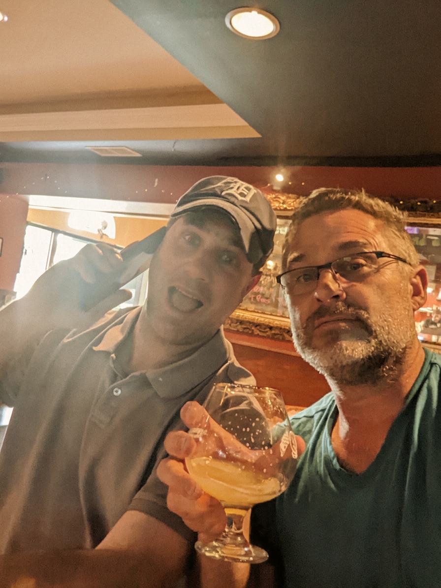 Russ (left, Tigers cap, phone to ear) and Todd (right, glasses) at a bar, warm editorial parchment tone